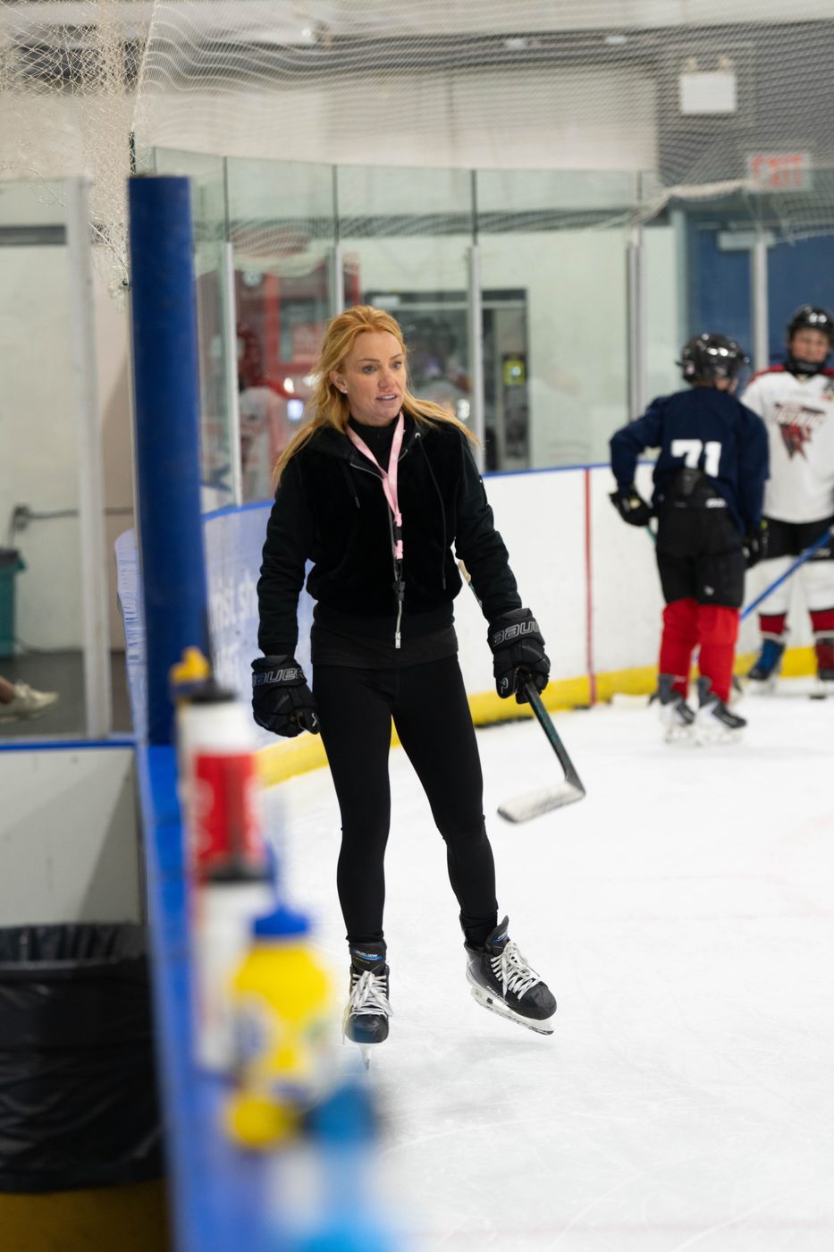 Stacy Allen on the ice with a group of young players on the bench behind her