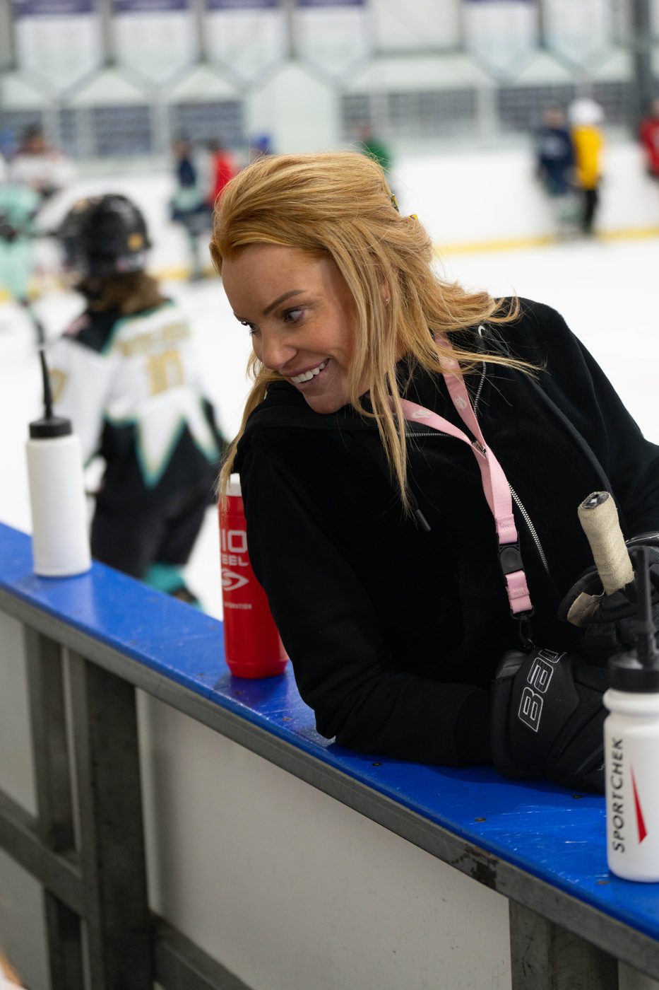 Stacy Allen smiling at the bench during a camp, players warming up behind her